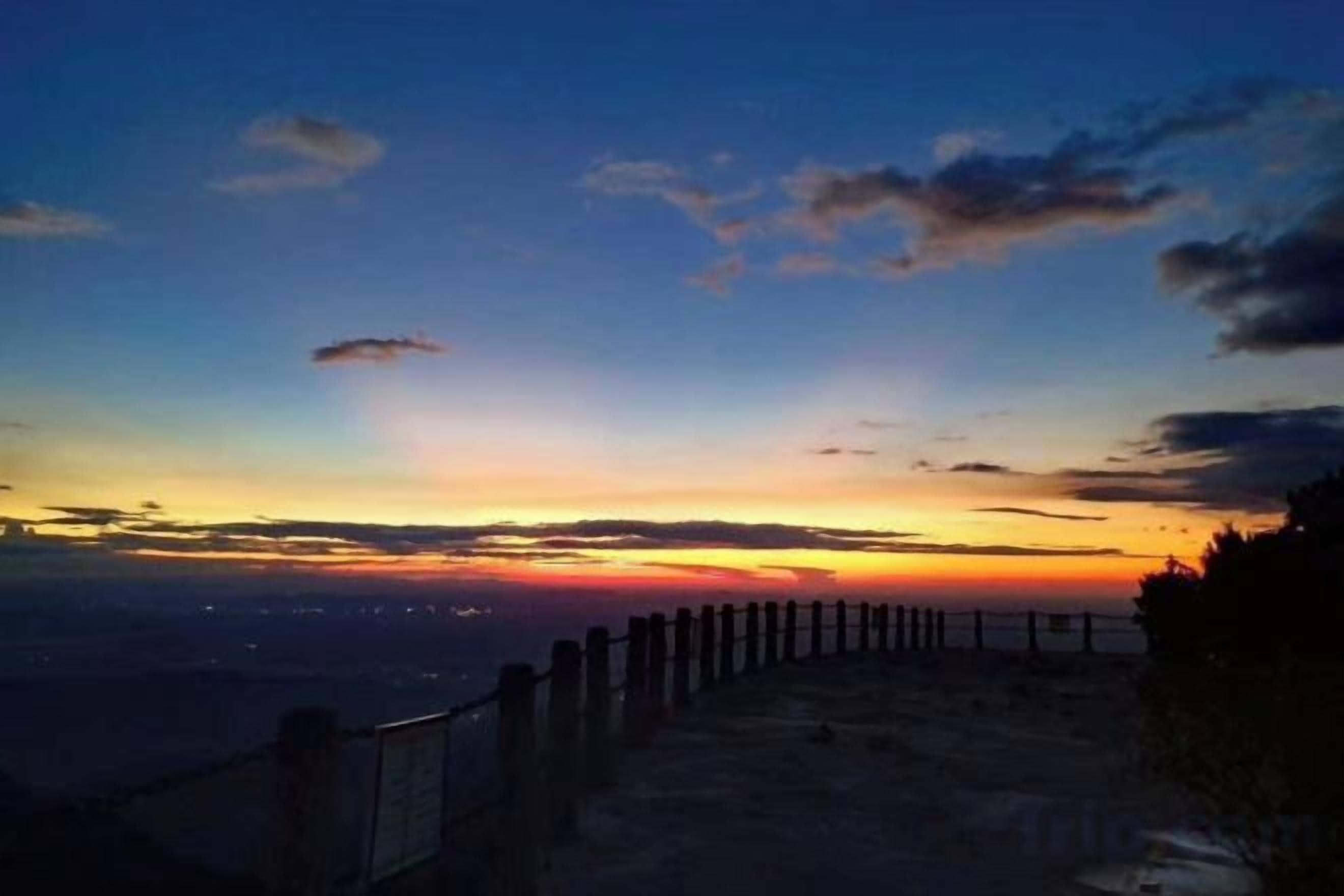 Vista al atardecer desde un lugar elevado, con una cerca de madera en primer plano.