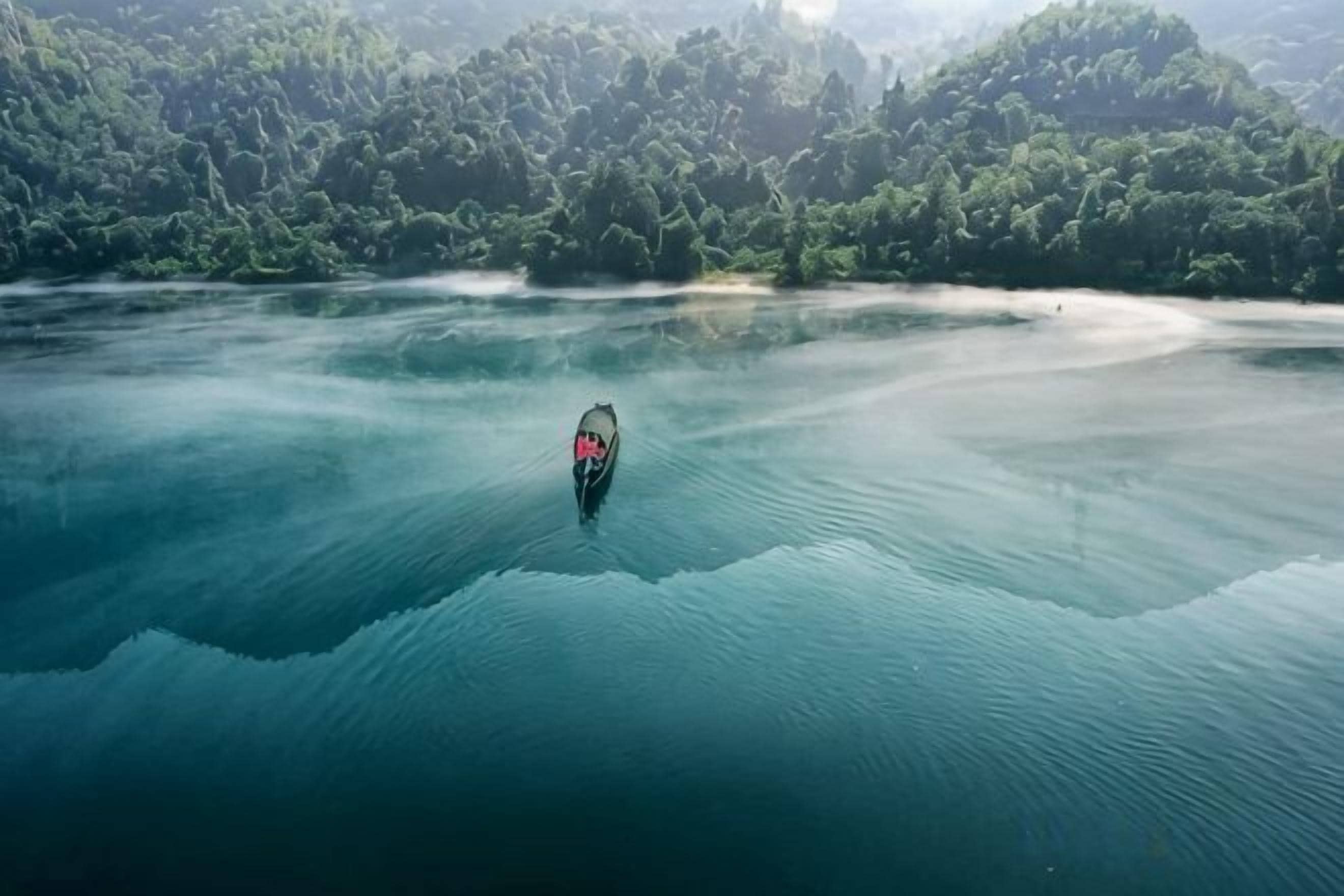 A boat on a calm body of water with a forested landscape in the background.