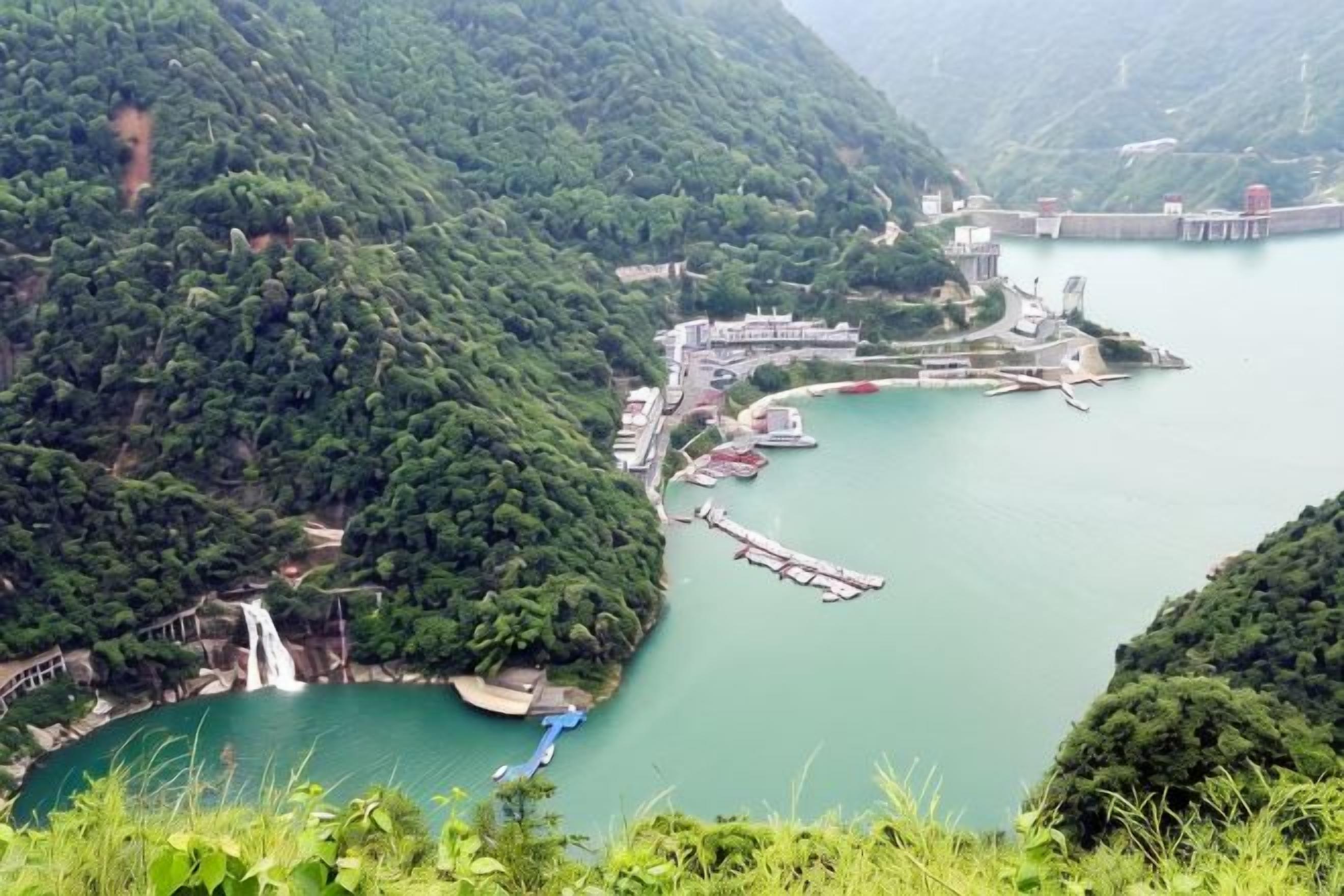 Un paisaje montañoso con un río, una cascada y un muelle con edificios.