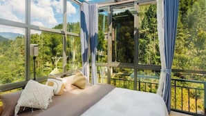 Une chambre avec un lit, des rideaux et une vue sur une forêt, visible à travers de grandes fenêtres.