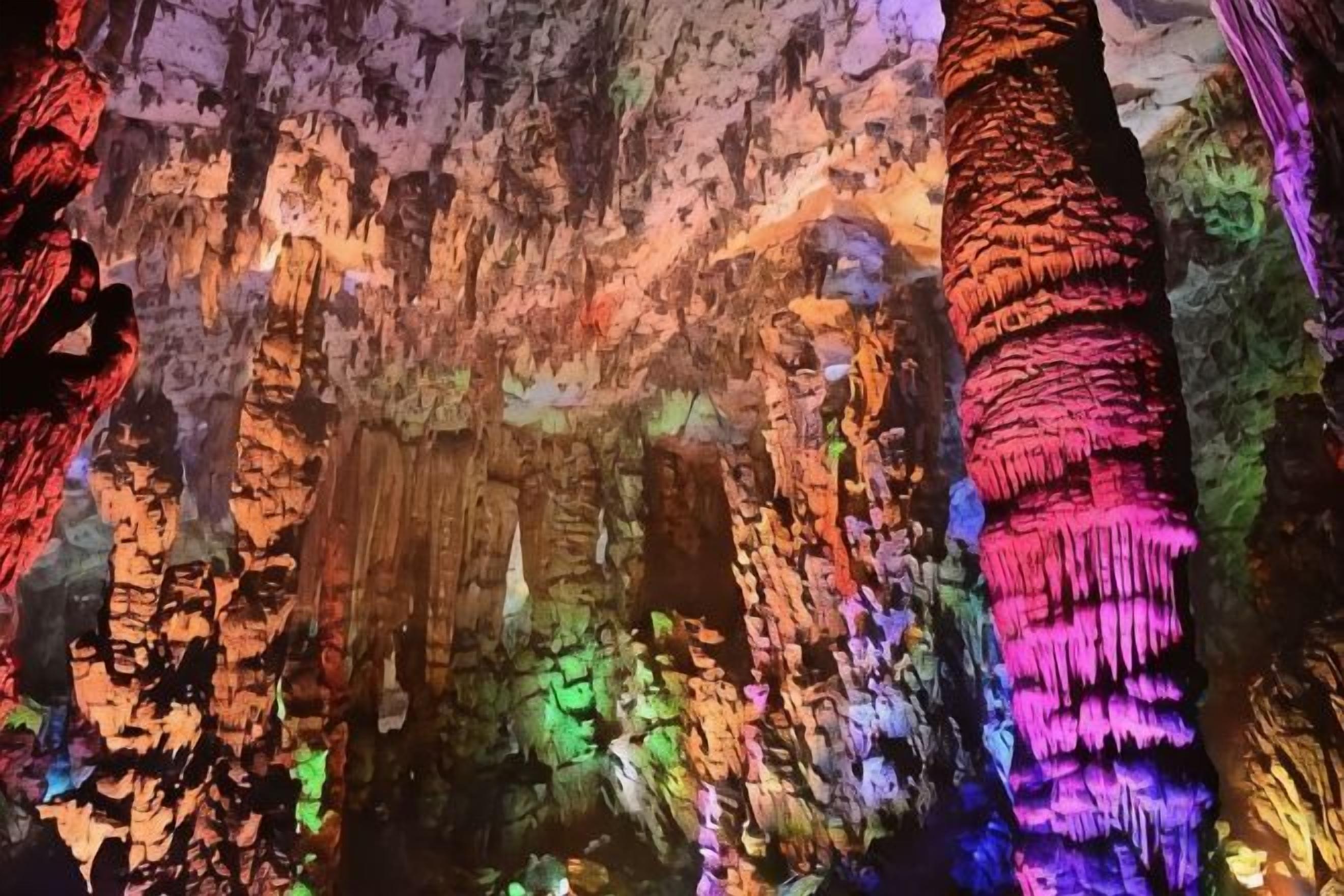 Una cueva con estalactitas iluminadas y una columna de formaciones rocosas.