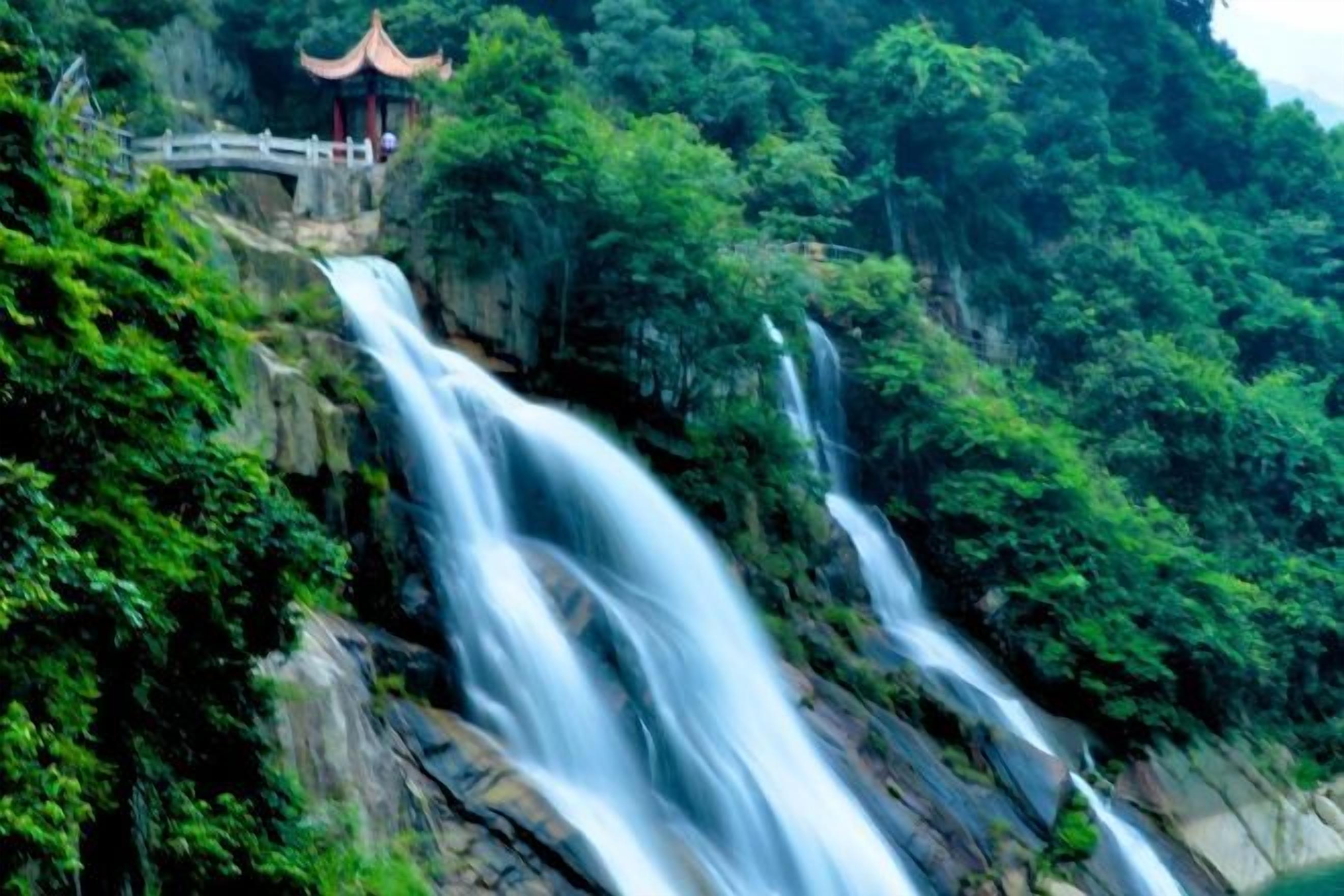 A waterfall cascading down a rocky cliff with lush greenery and a traditional pavilion.