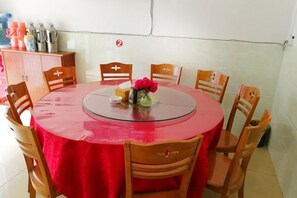 A round table with a red tablecloth, surrounded by wooden chairs, and a vase with flowers on the table.
