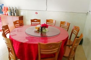 Una mesa redonda con mantel rojo, rodeada de sillas de madera, y un florero con flores sobre la mesa.
