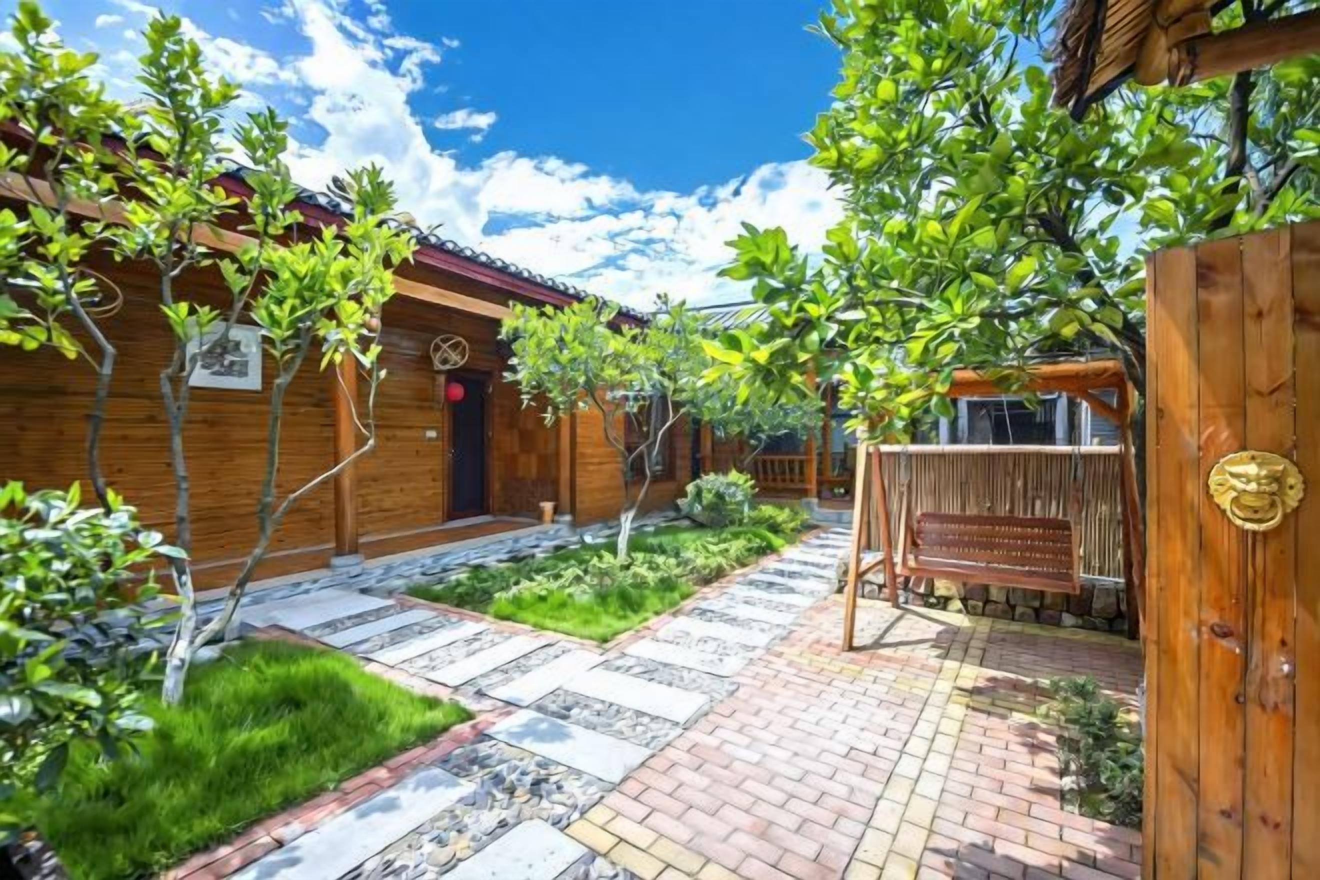 A courtyard with wooden buildings, a paved walkway, and a wooden gate.