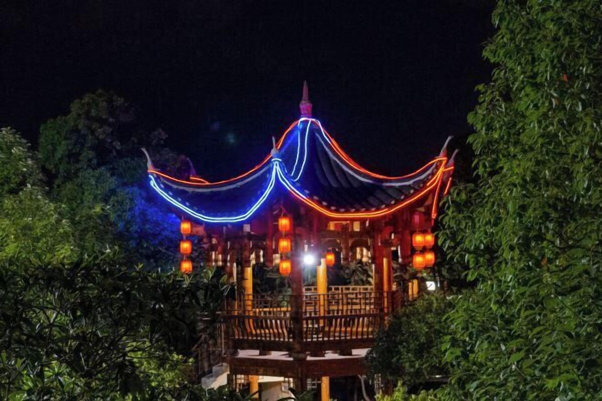 Ein traditioneller chinesischer Pavillon mit gewölbter Dachform, umgeben von üppigem Grün.