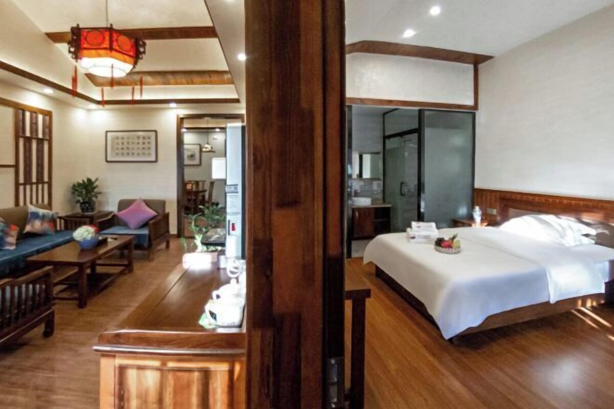 Ein Hotelzimmer mit Holzboden, einem Bett mit weißer Bettwäsche, einem Holz-Kopfteil, einem Nachttisch und einem kleinen Tisch mit einer Vase und einer Kerze.