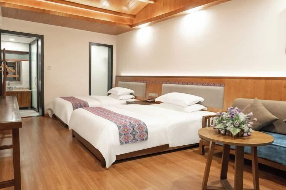 Hotellihuone, jossa on puinen katto, suuri sänky valkoisilla vuodevaatteilla, pieni pyöreä pöytä, jossa on kukka-asetelma, ja tyynyillä varustettu sohva.