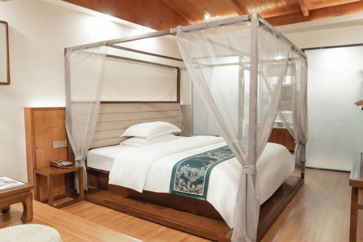 Ein Schlafzimmer mit Himmelbett, Holz-Kopfteil, Nachttischen und einem Beistelltisch.