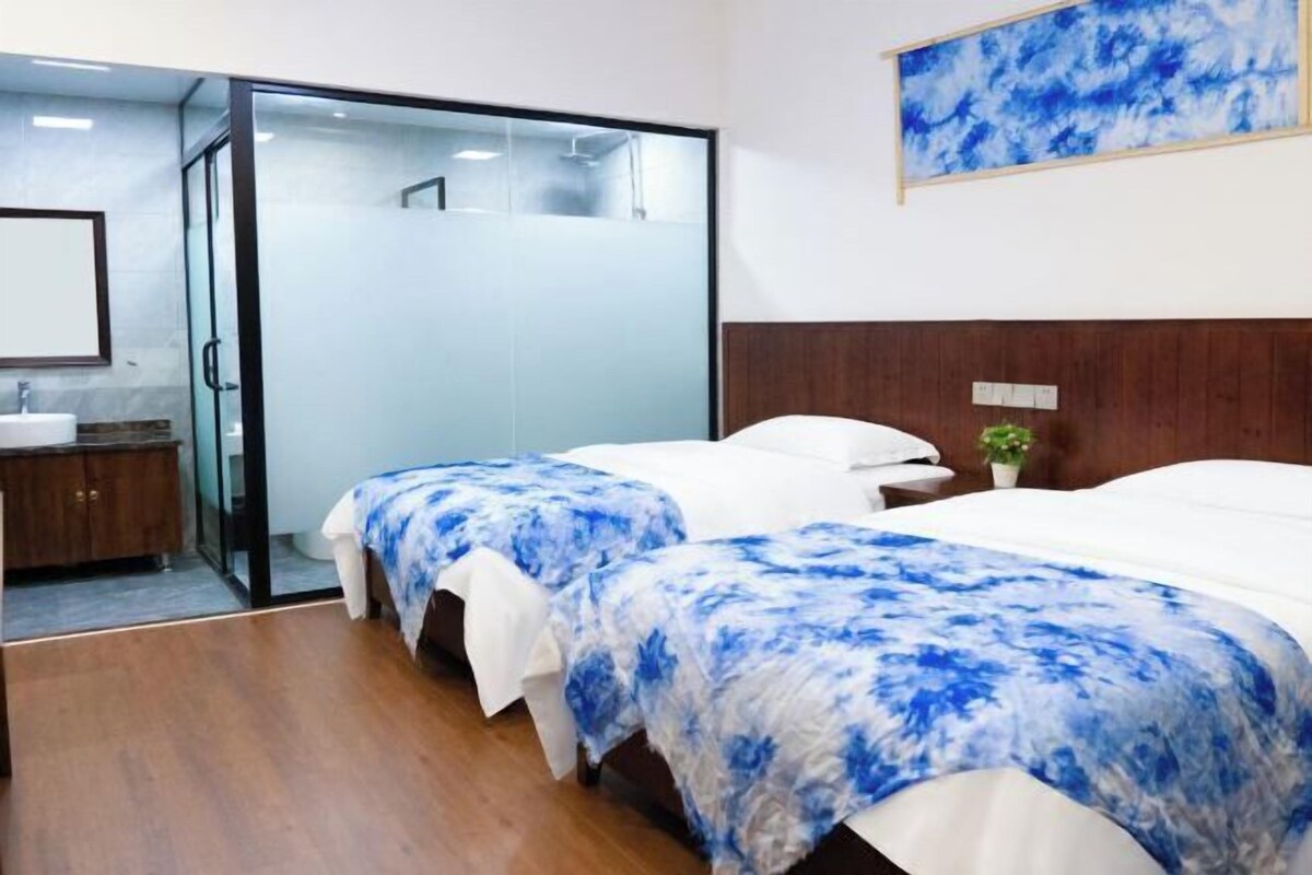 Ein Hotelzimmer mit zwei Betten, einer Glasdusche, einem Holzkopfteil und einem Bild an der Wand.