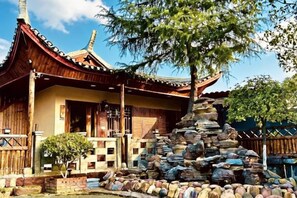 Un edificio tradicional con techo de tejas y estructura de madera, rodeado de un jardín de piedra con una formación rocosa central.