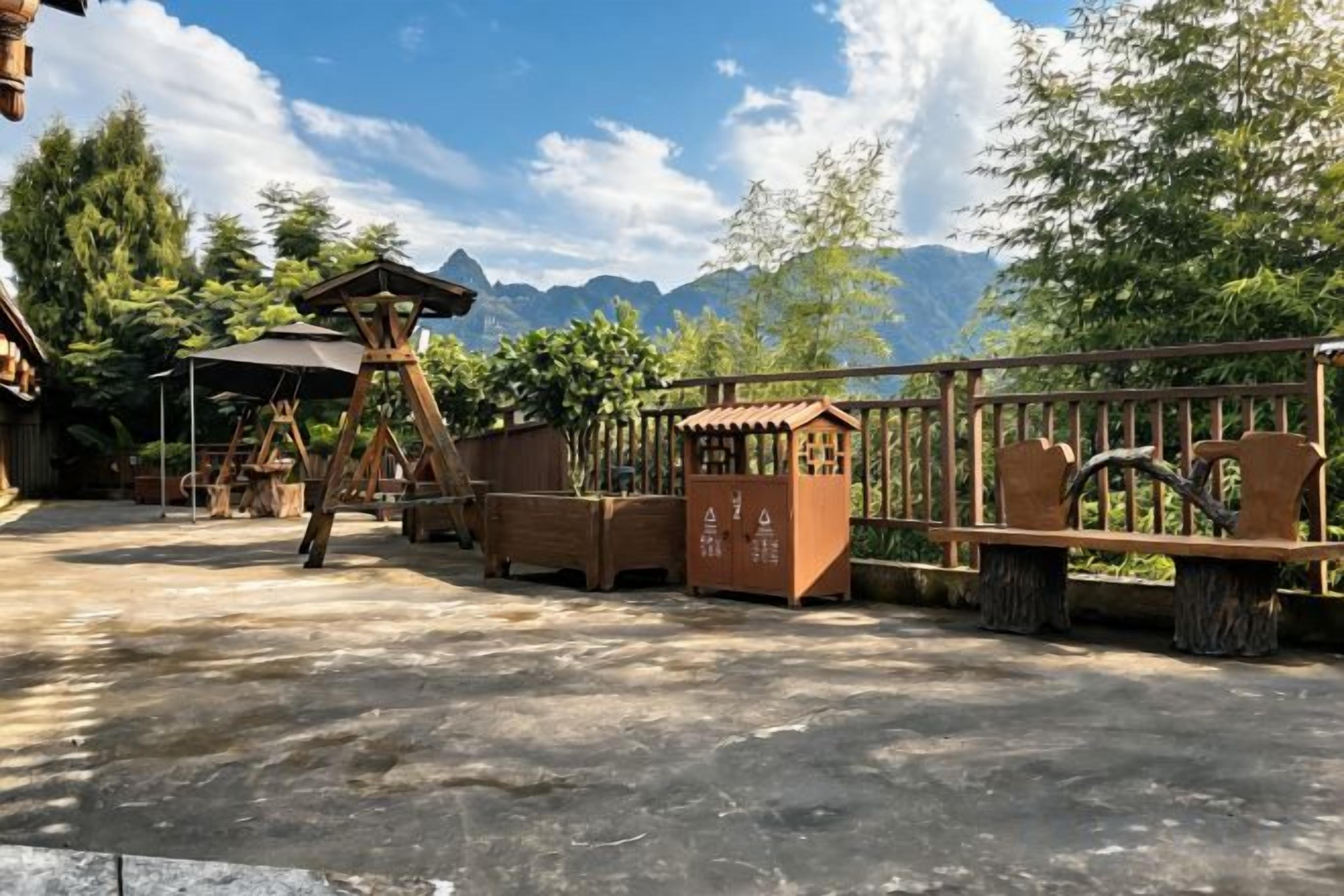 A wooden outdoor area with a swing set, a small shelter, and a fenced play area with a view of mountains.
