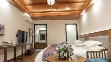 Habitación de hotel con techo de madera, cama con edredón estampado, mesa redonda con un jarrón de flores y televisor sobre un mueble.