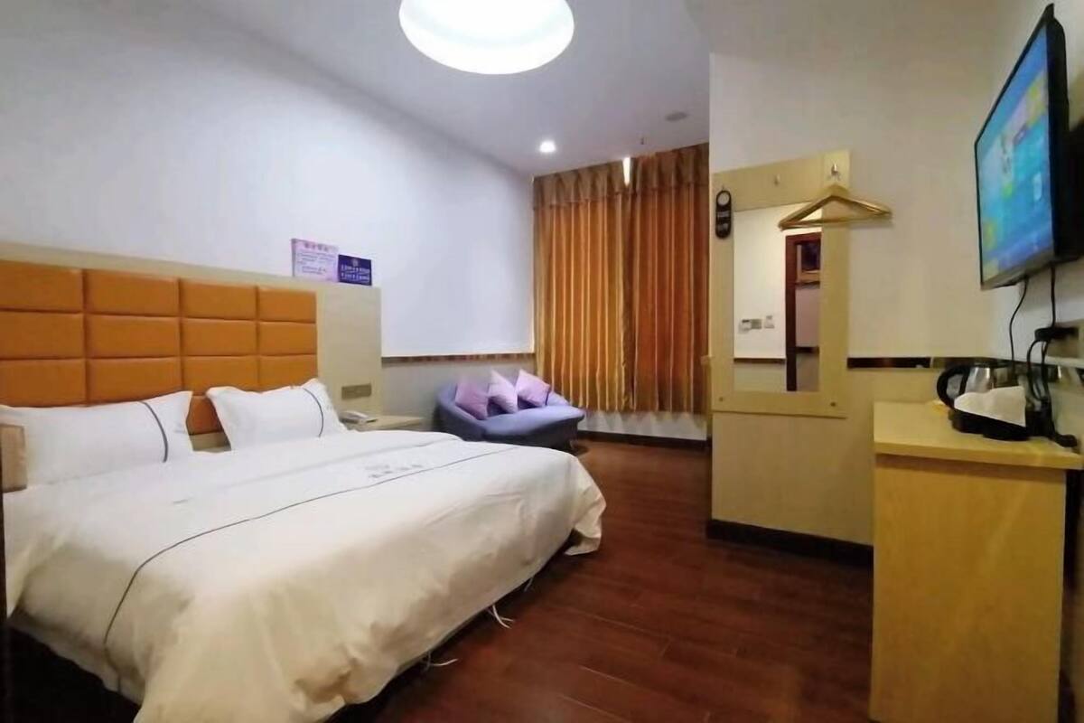 A hotel room with a bed, a desk, a chair, a television, and a bathroom mirror.