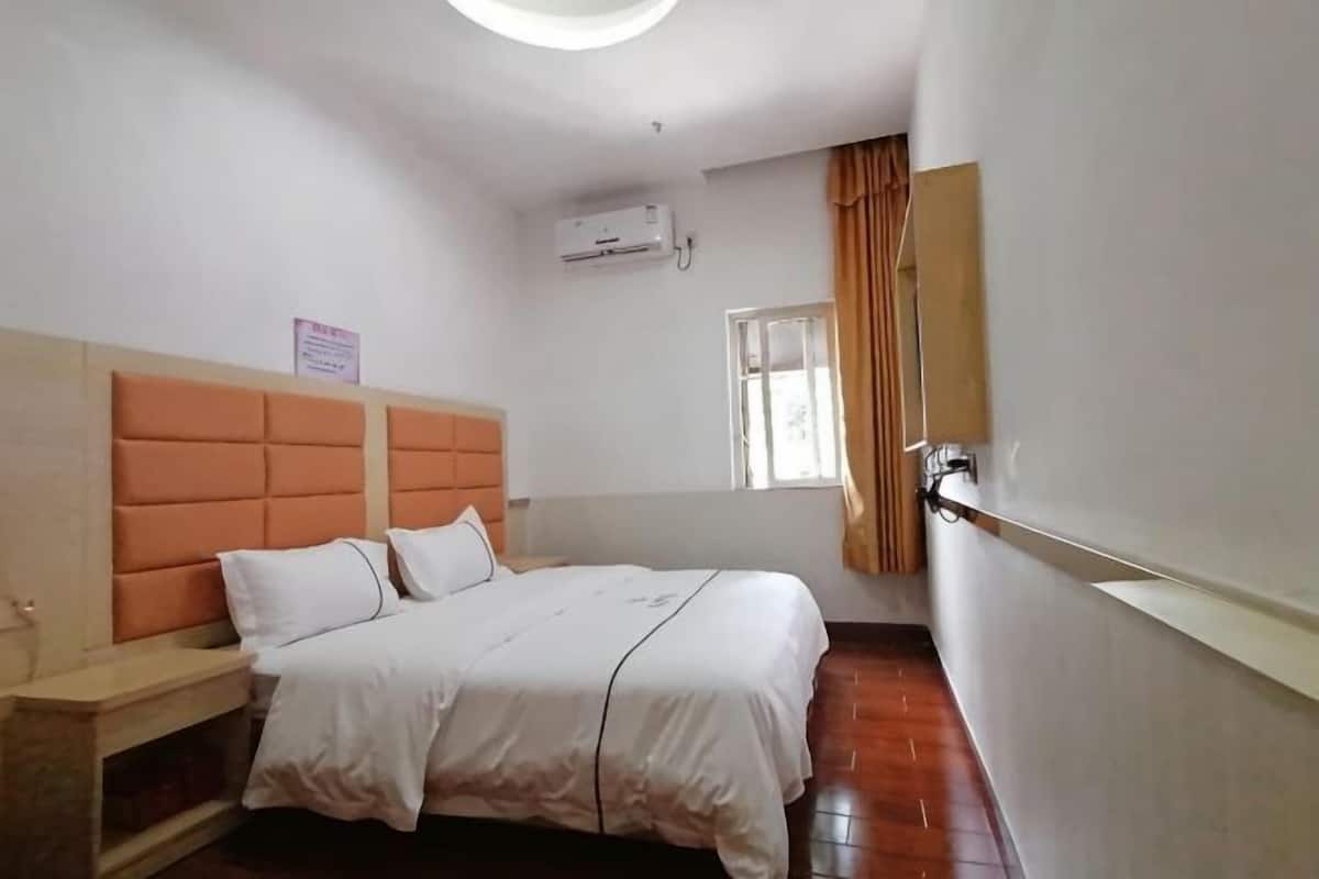 A bedroom with a bed, a nightstand, a window with curtains, and an air conditioning unit.