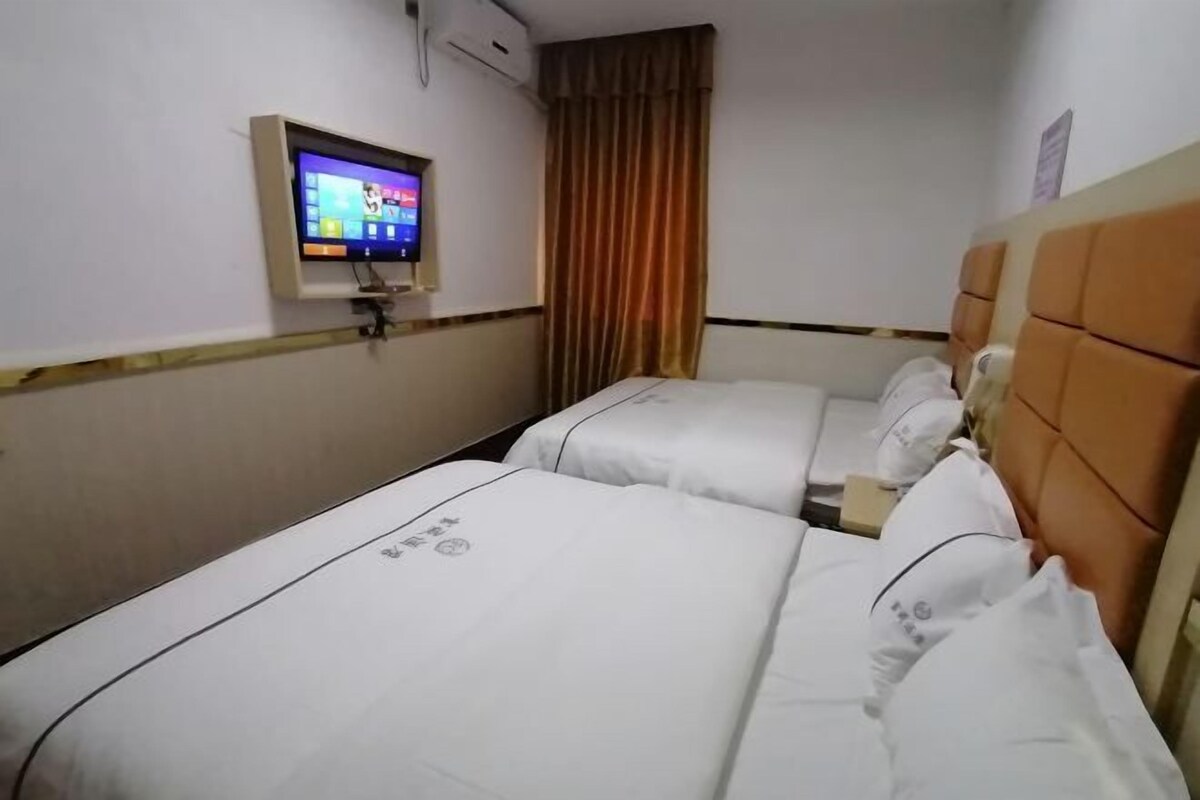 Ein Hotelzimmer mit zwei Betten, einem an der Wand befestigten Fernseher und einem Fenster mit Vorhängen.