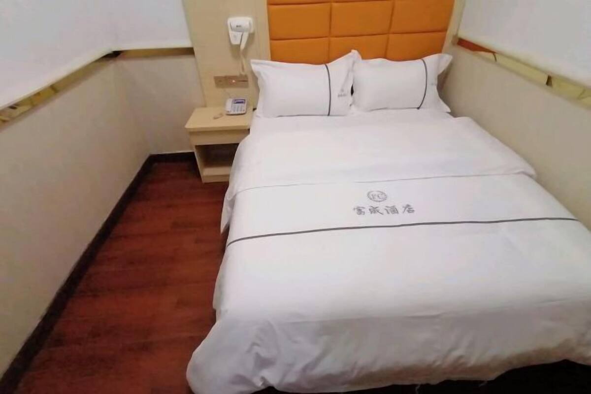 A hotel room with a bed, a nightstand, a phone, and a wall socket.