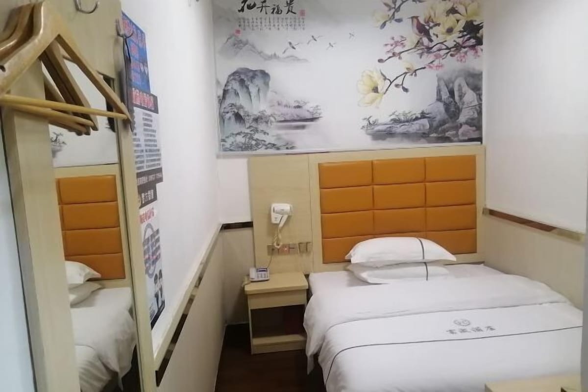 Ein Hotelzimmer mit Bett, Nachttisch, Spiegel und einer Wand mit Blumenbild.