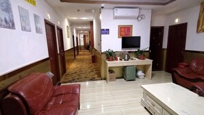 Vestíbulo de hotel con una recepción, un televisor, un sofá y un largo pasillo.