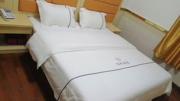 Una cama bien hecha con ropa de cama y almohadas blancas, un teléfono en la mesita de noche y una mesita de madera.