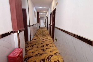 Un couloir d’hôtel avec un tapis à motifs, des murs en marbre et des portes donnant accès aux chambres.