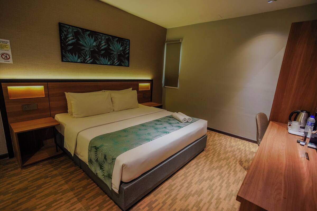 A hotel room with a bed, bedside tables, a desk, a chair, a painting, and a mirror.