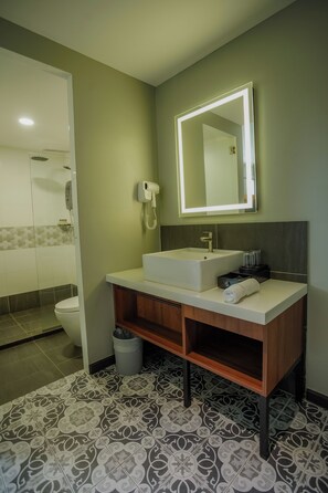 Un baño con un lavamanos blanco, un espejo con iluminación y un secador de pelo, además de baldosas de suelo con diseño.