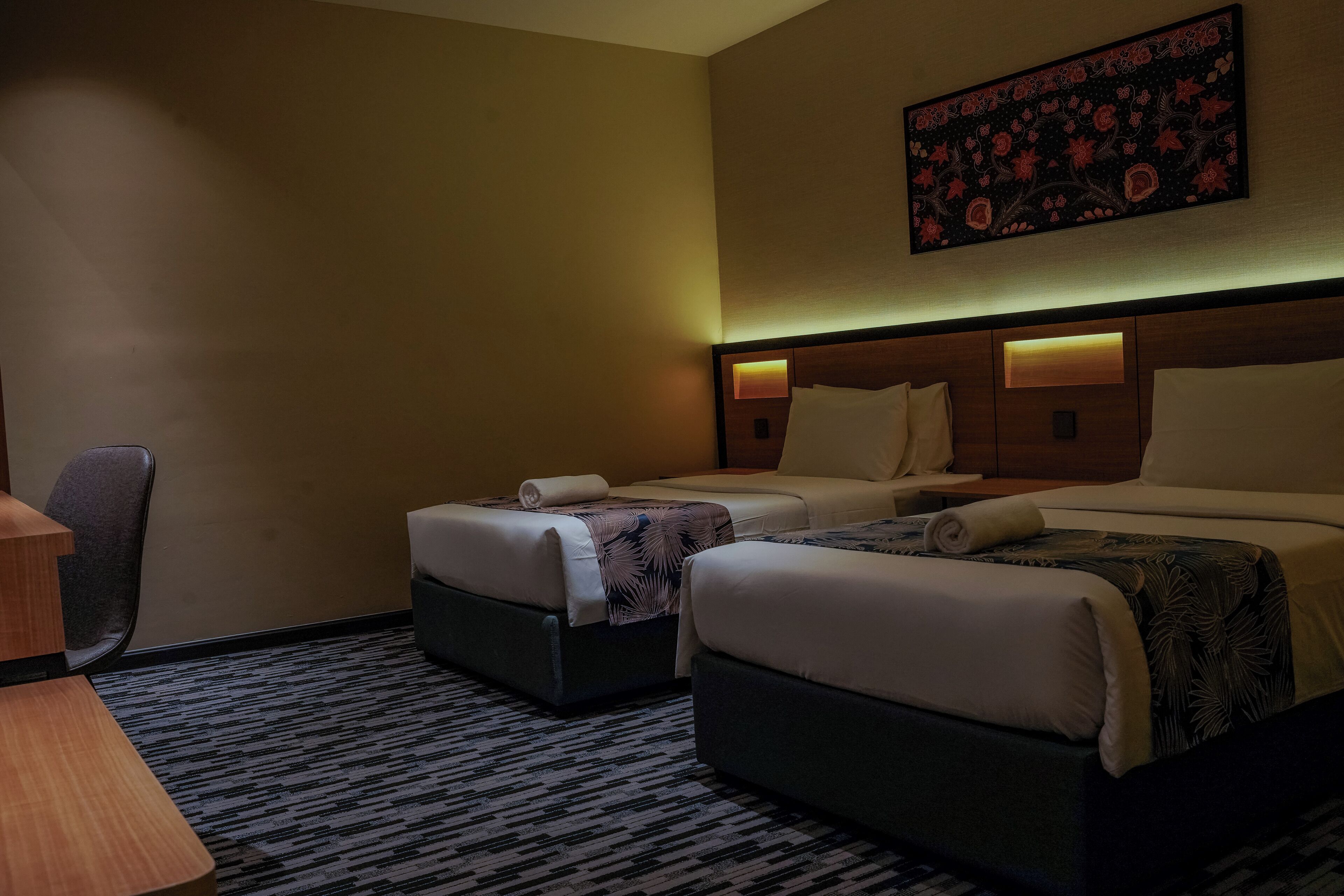 A hotel room with two beds, a desk, and a chair.