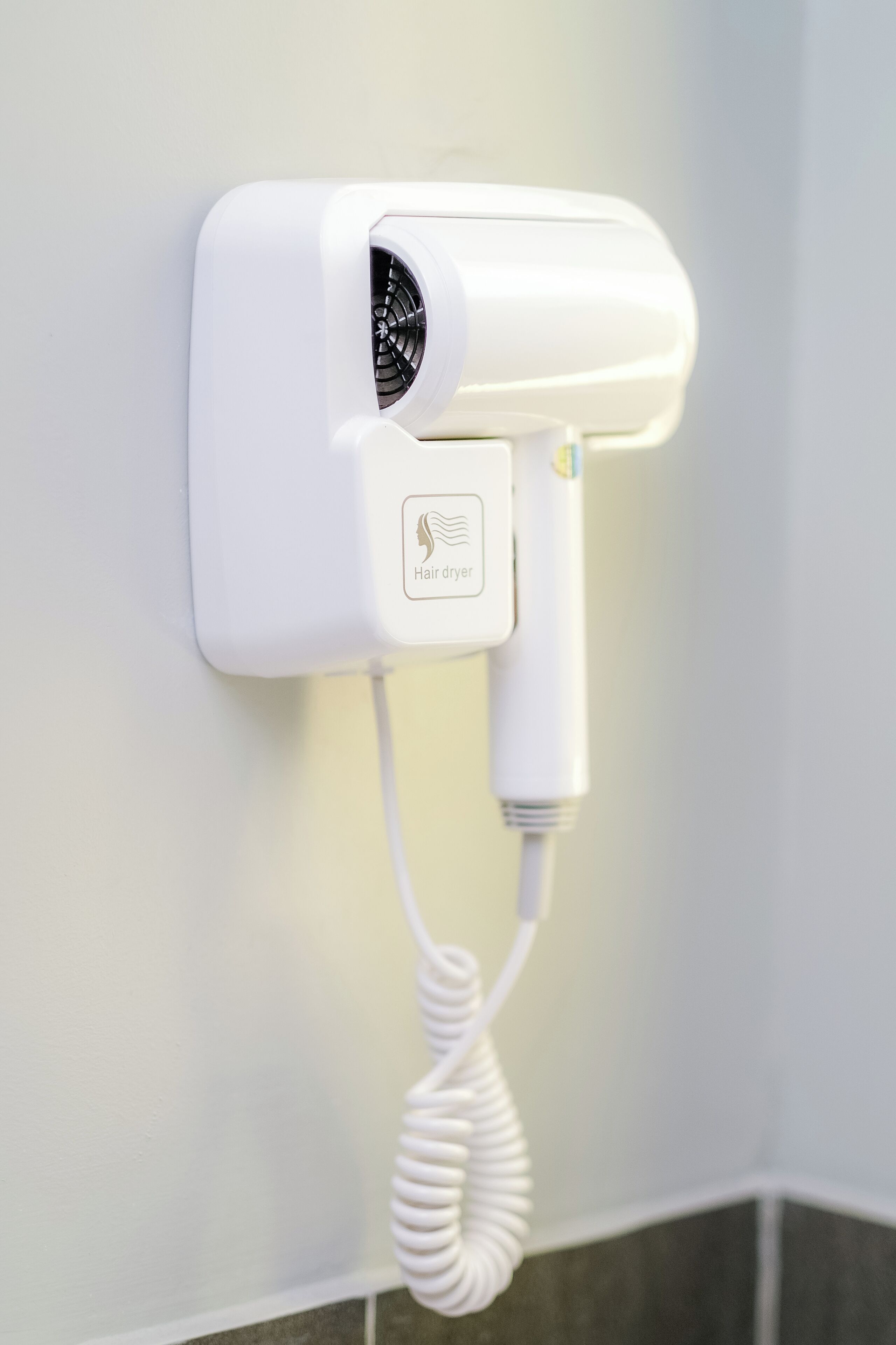 A hair dryer mounted on a wall with a coiled cord.