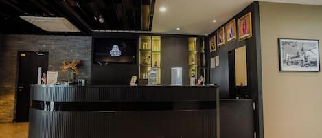 A reception area with a modern design, featuring a black reception desk, a flat-screen TV, and a wall-mounted display.