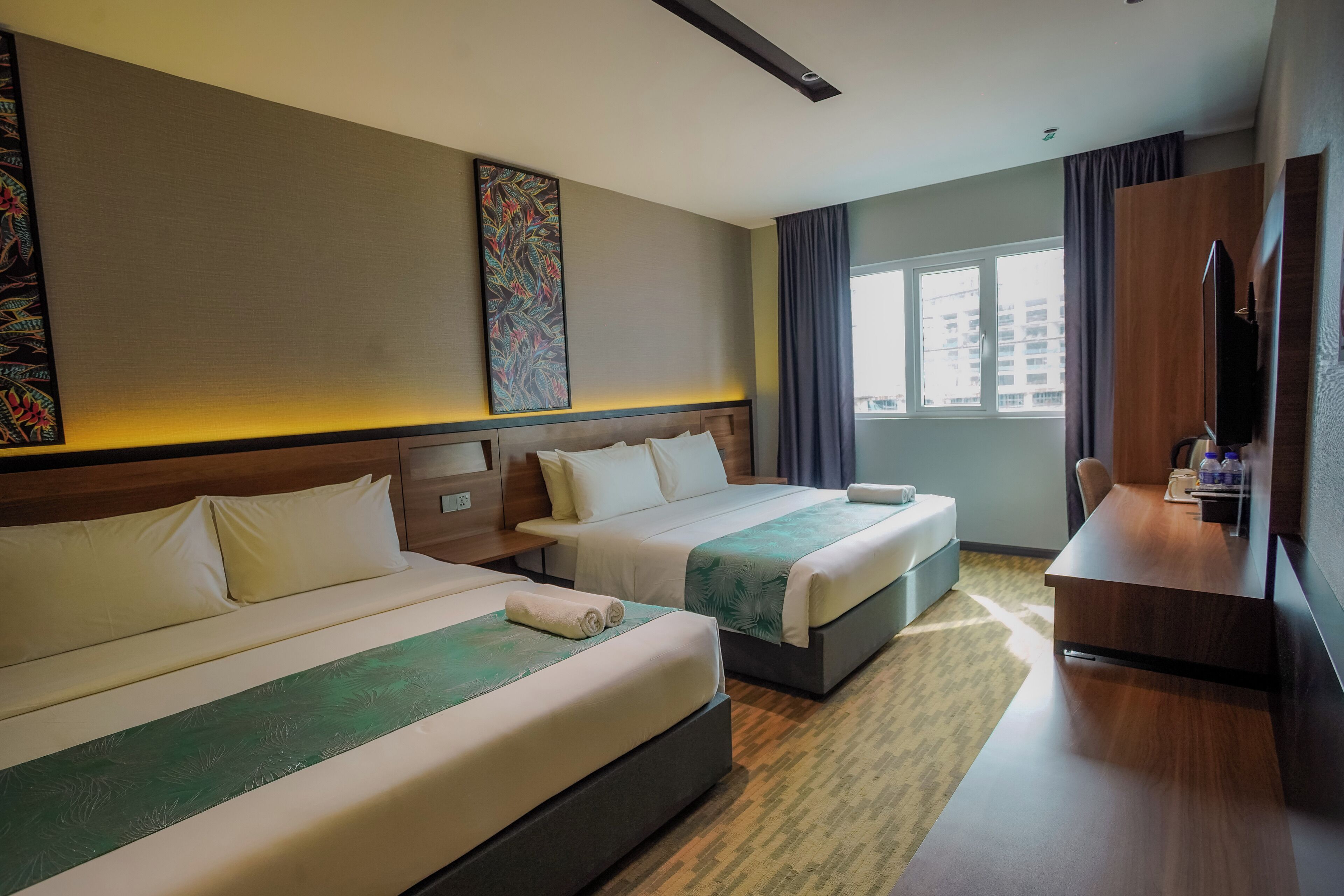 Een hotelkamer met twee bedden, een bureau, een televisie en een groot raam.