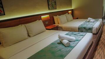Habitación de hotel con dos camas, cada una con cubrecama estampado con hojas verdes, almohadas blancas y toallas dobladas con cuidado.