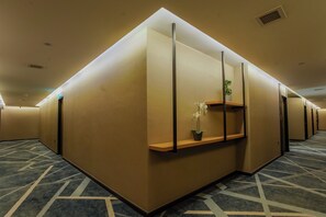 Zona de recepción de hotel con un diseño moderno, que incluye un mostrador de recepción, una planta en maceta y una alfombra estampada.