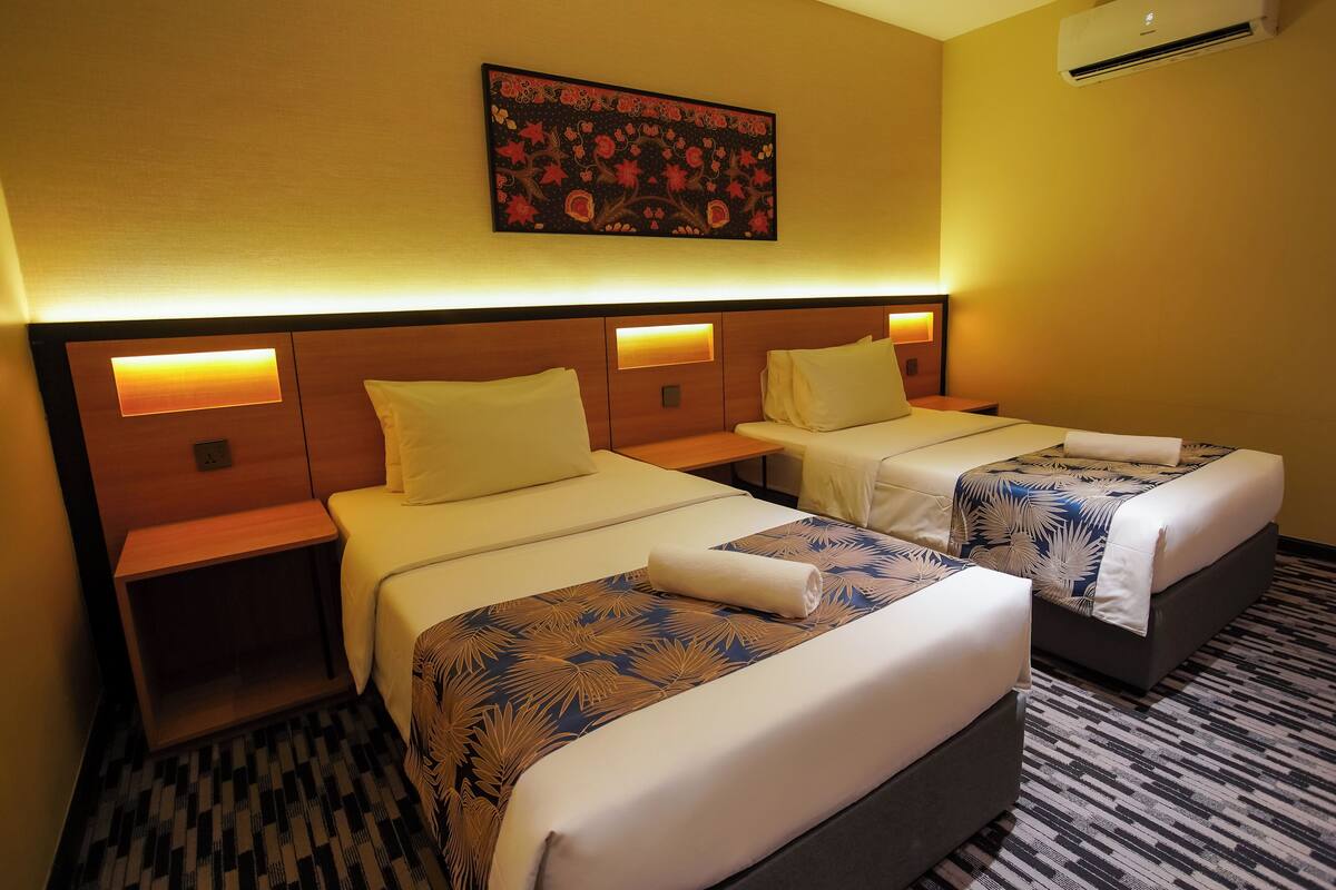 A hotel room with two beds, each with a headboard, bedside tables, and a wall-mounted air conditioner.
