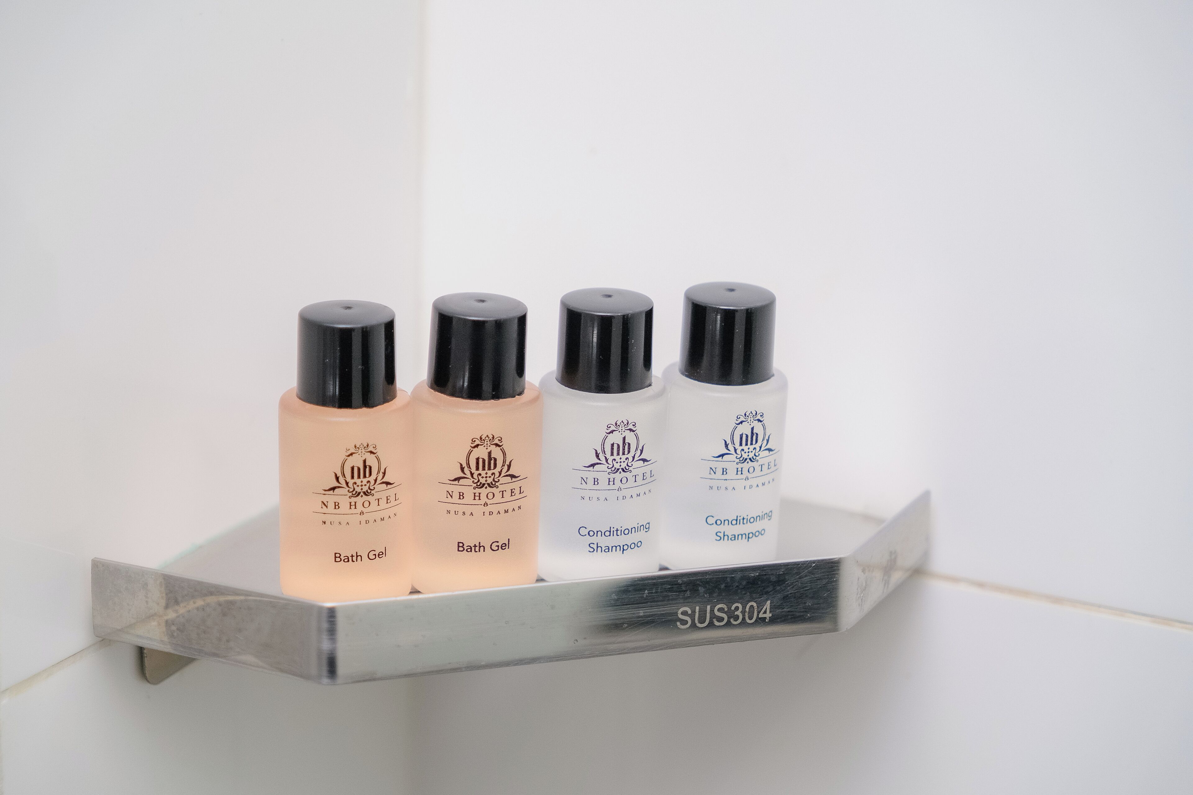 Un estante en el baño con cuatro productos de Nusa Iraman: gel de baño, champú acondicionador y champú acondicionador.