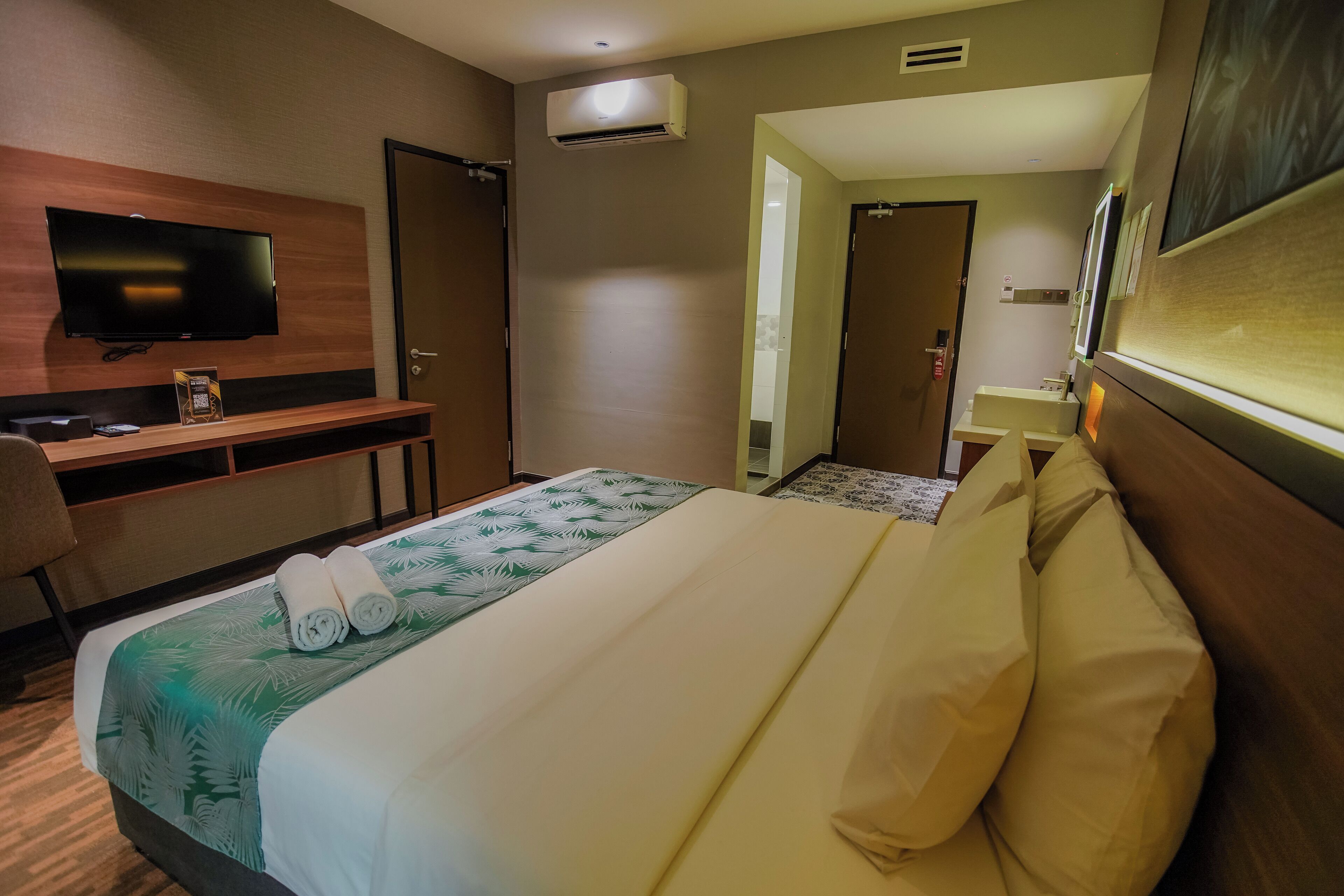 Une chambre d’hôtel équipée d’un lit, d’un bureau avec un téléviseur à écran plat, d’une chaise et d’un appareil de climatisation.