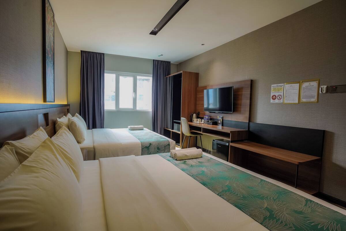 A hotel room with two beds, a desk, a TV, and a window.