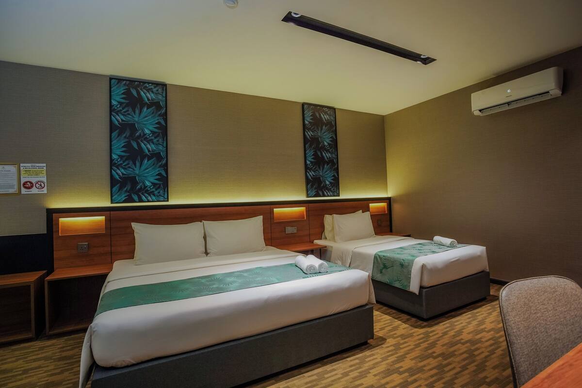 A hotel room with two beds, a desk, and a chair. There is an air conditioning unit on the wall and a wall-mounted artwork above the beds.