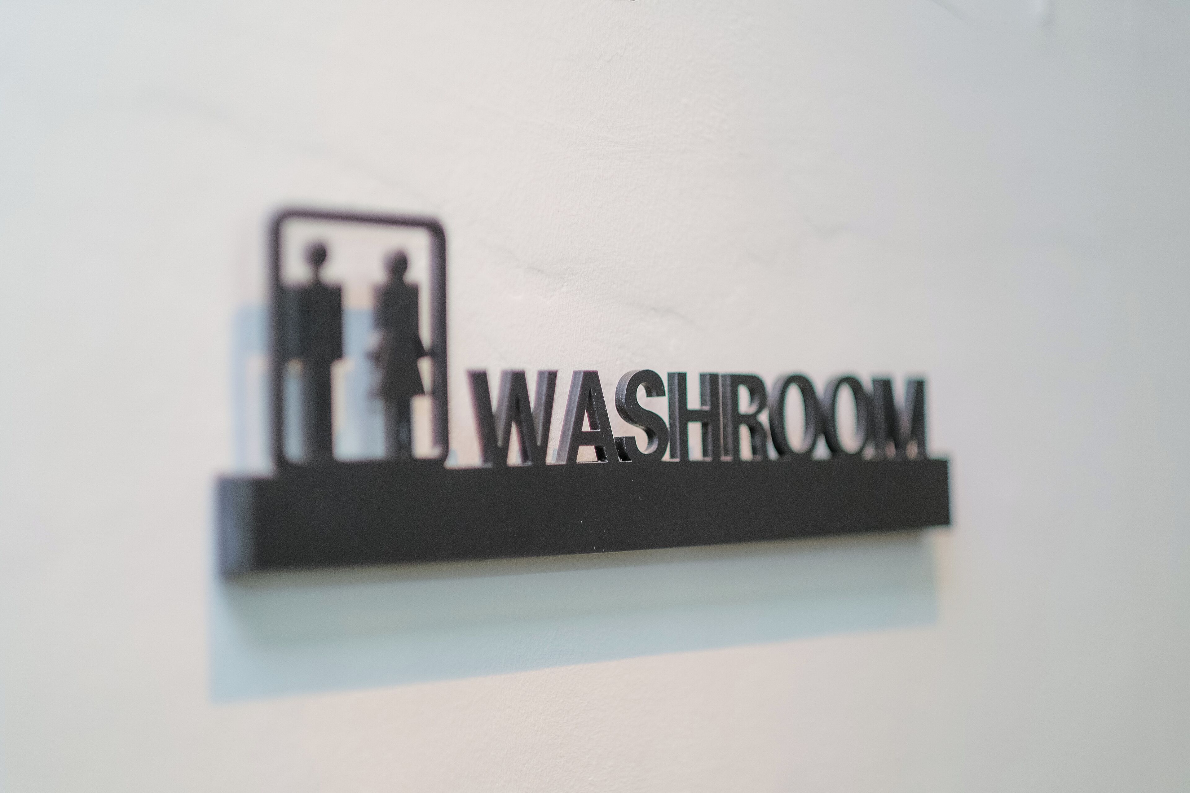 Un letrero con la palabra 'WASHROOM' y la silueta de dos personas.
