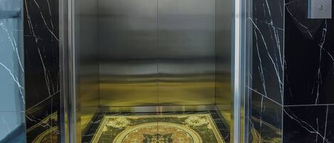 Un ascensor con suelo y paredes de mármol, una pantalla digital e iluminación en el techo.