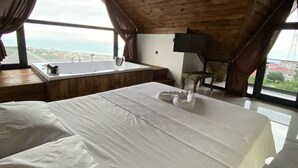 Quarto com uma cama grande, teto de madeira e vista para o mar.