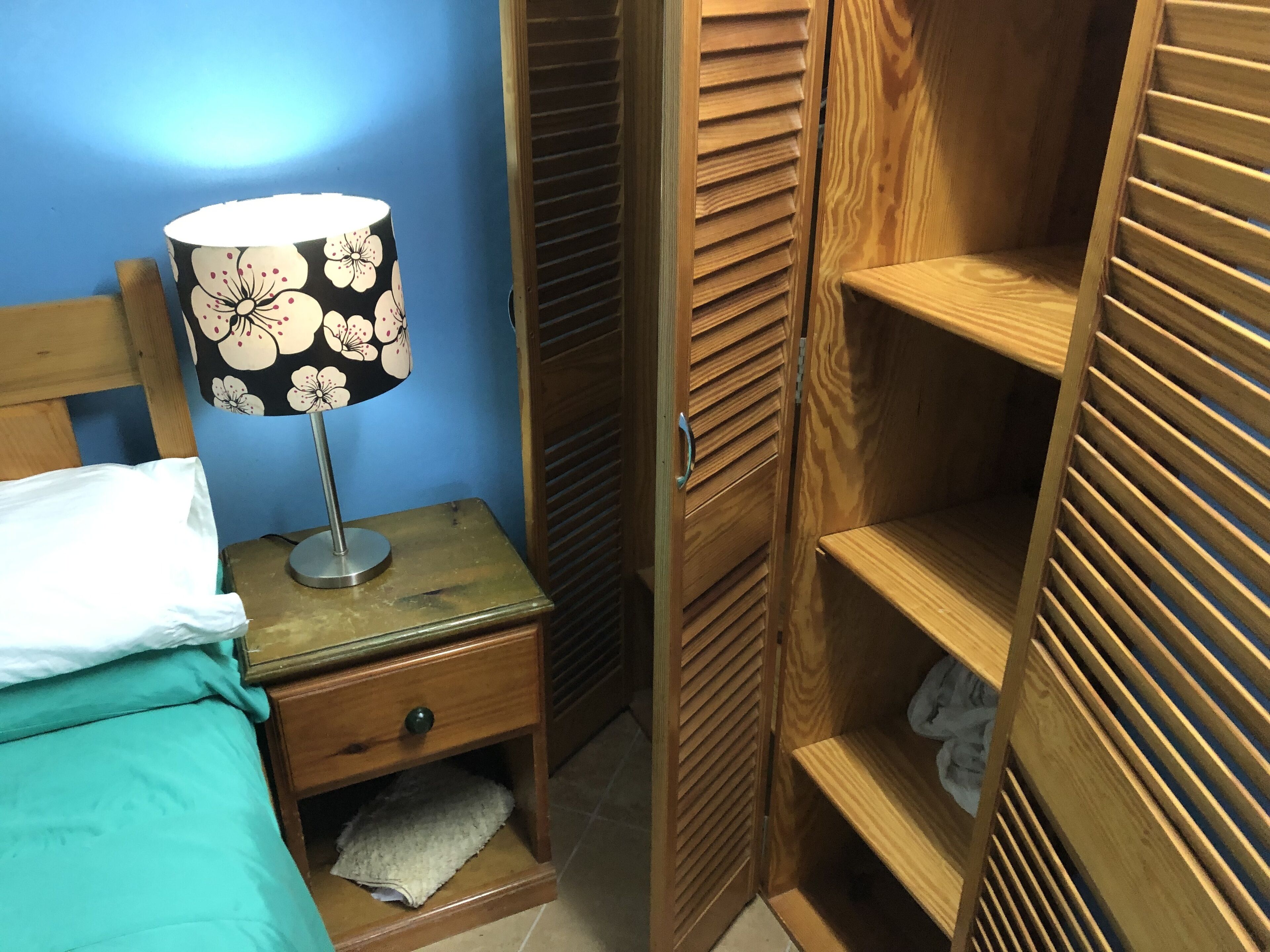 Un dormitorio con cama, mesita de noche con lámpara y estanterías de madera.