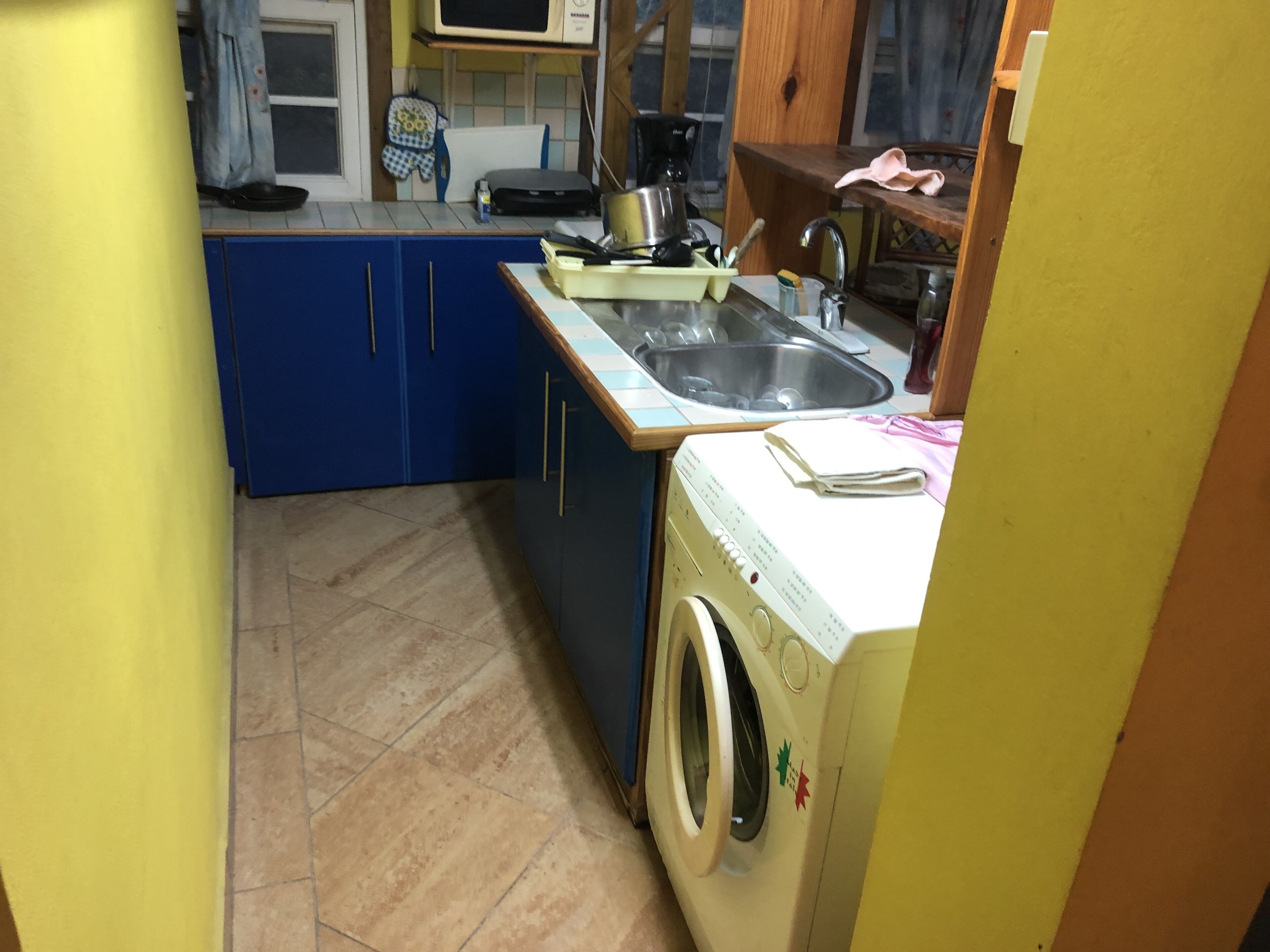 Een kleine keuken met blauwe kastjes, een wasmachine en een spoelbak.
