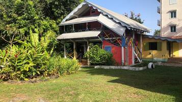 A two-story building with a red and white exterior, a covered porch, and a small garden area with tropical plants.