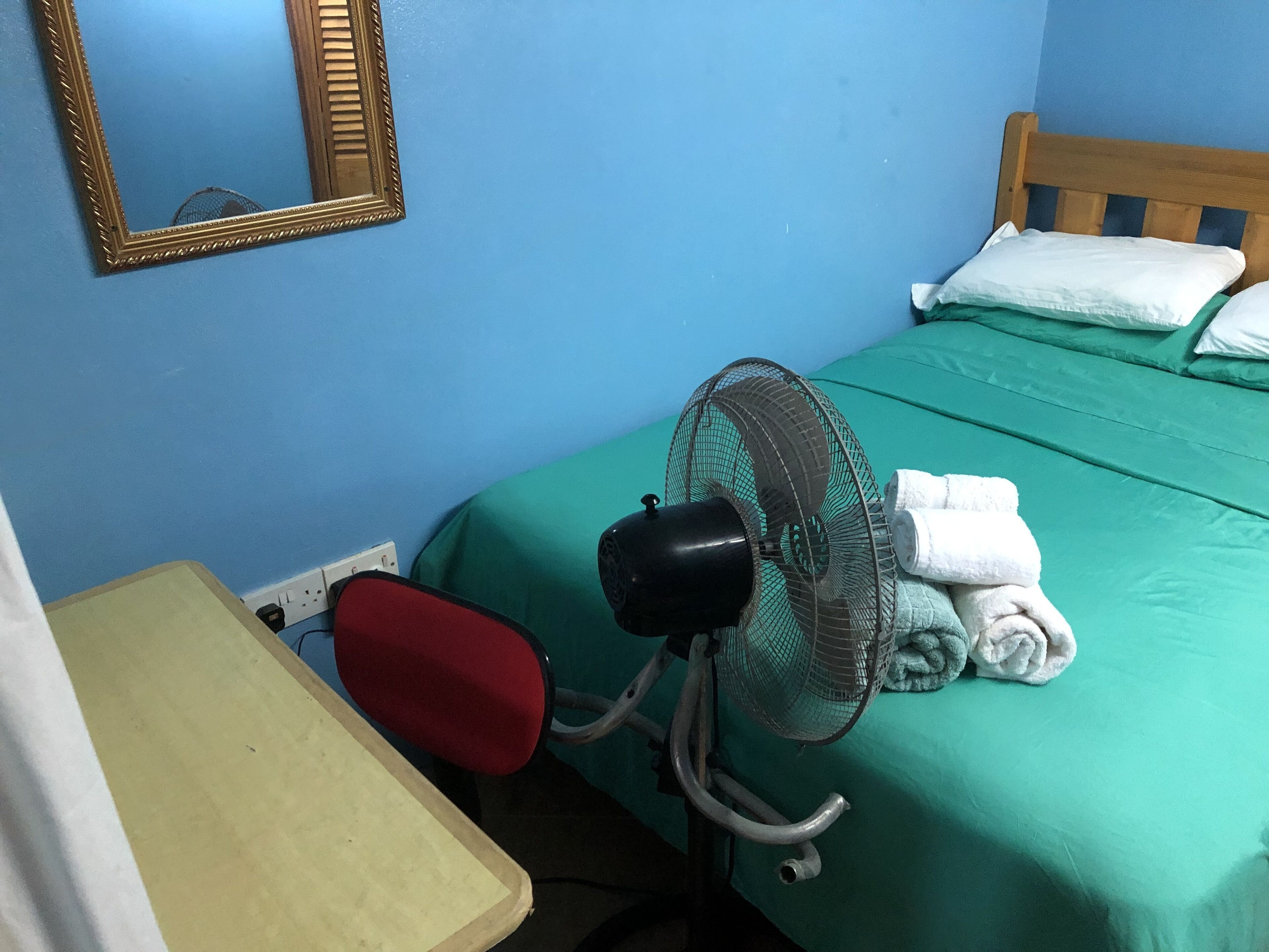 Una habitación con cama, ventilador, mesa y espejo.