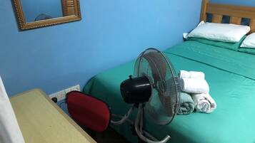 Una habitación con cama, ventilador, mesa y espejo.