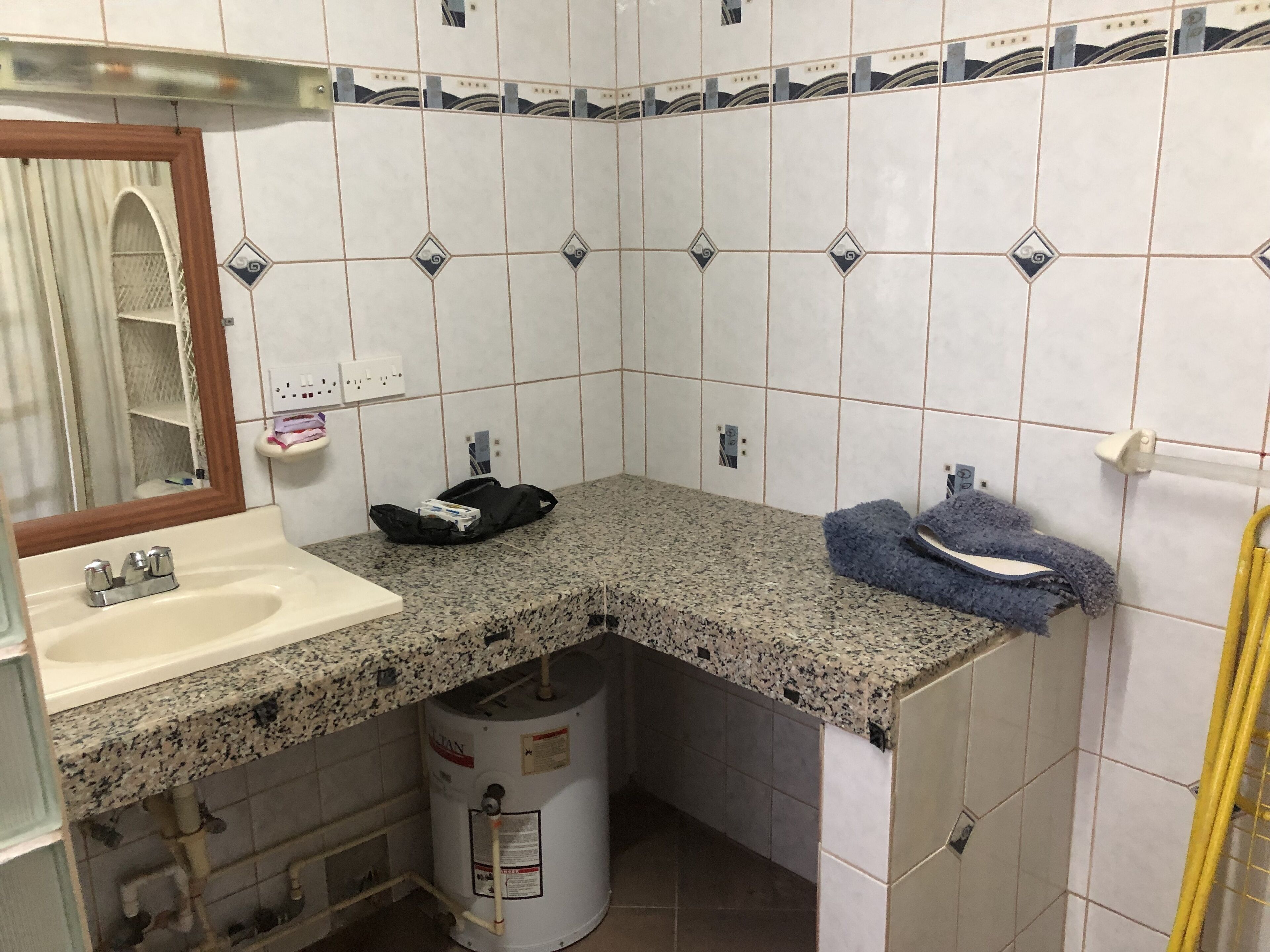 A bathroom with a granite countertop sink, a mirror, a towel rack, and a water heater.