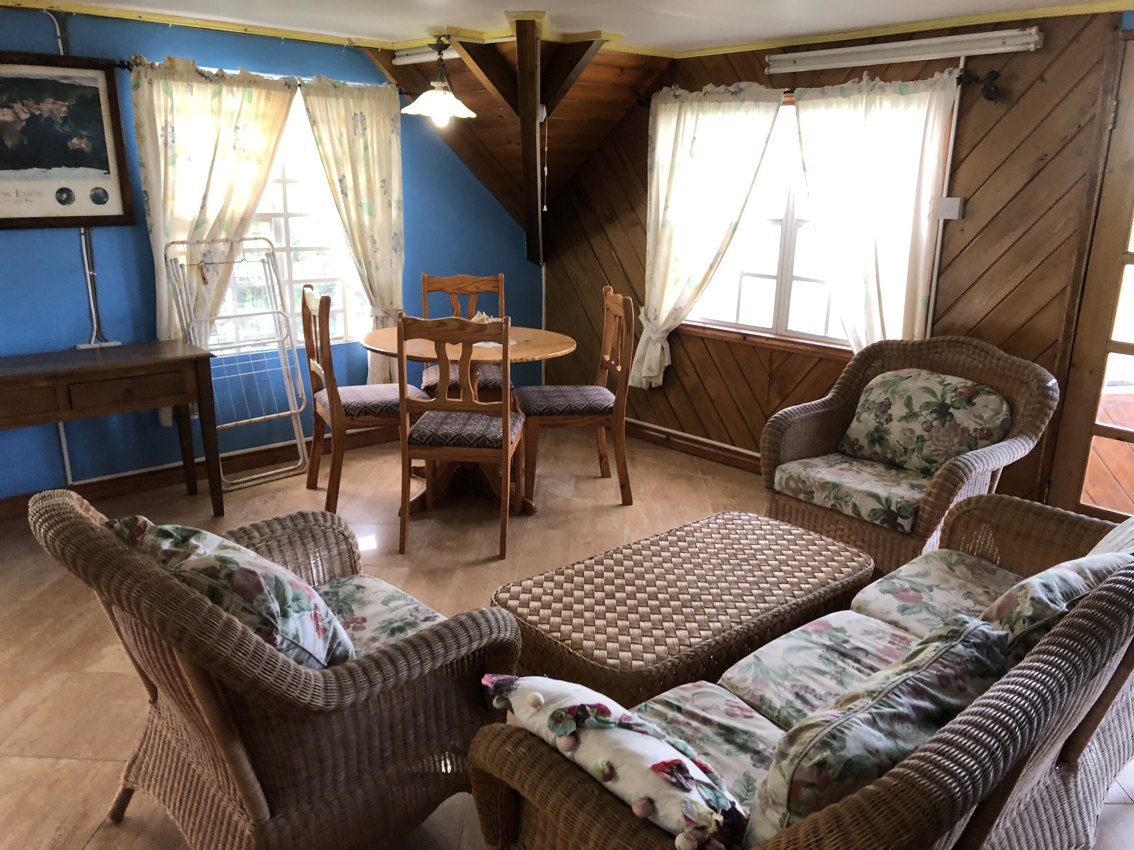 A cozy room with a wooden ceiling, a round table with chairs, wicker furniture, and floral-patterned cushions.