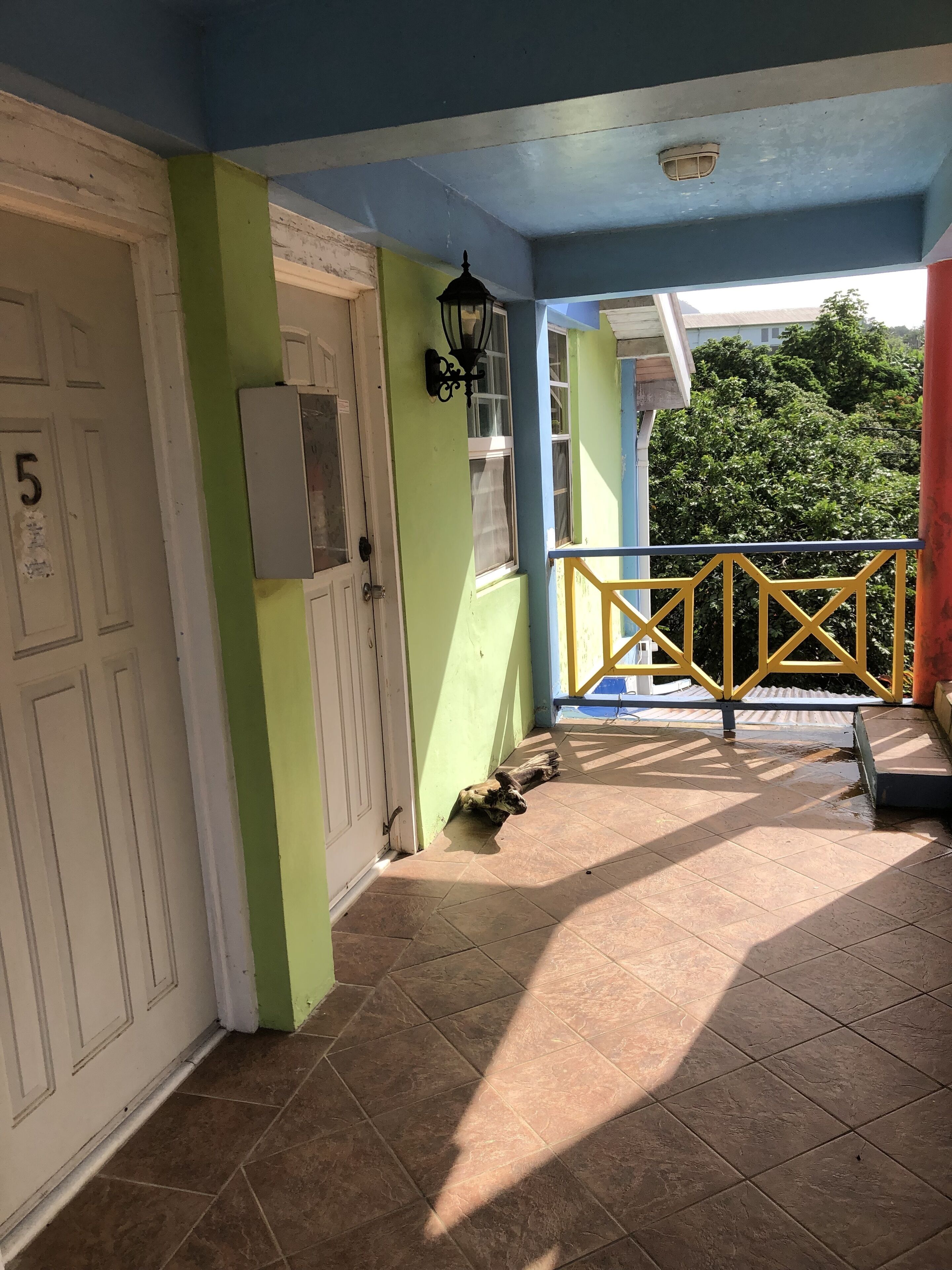 A covered porch with a tiled floor, a yellow railing, and a door marked with the number 5.