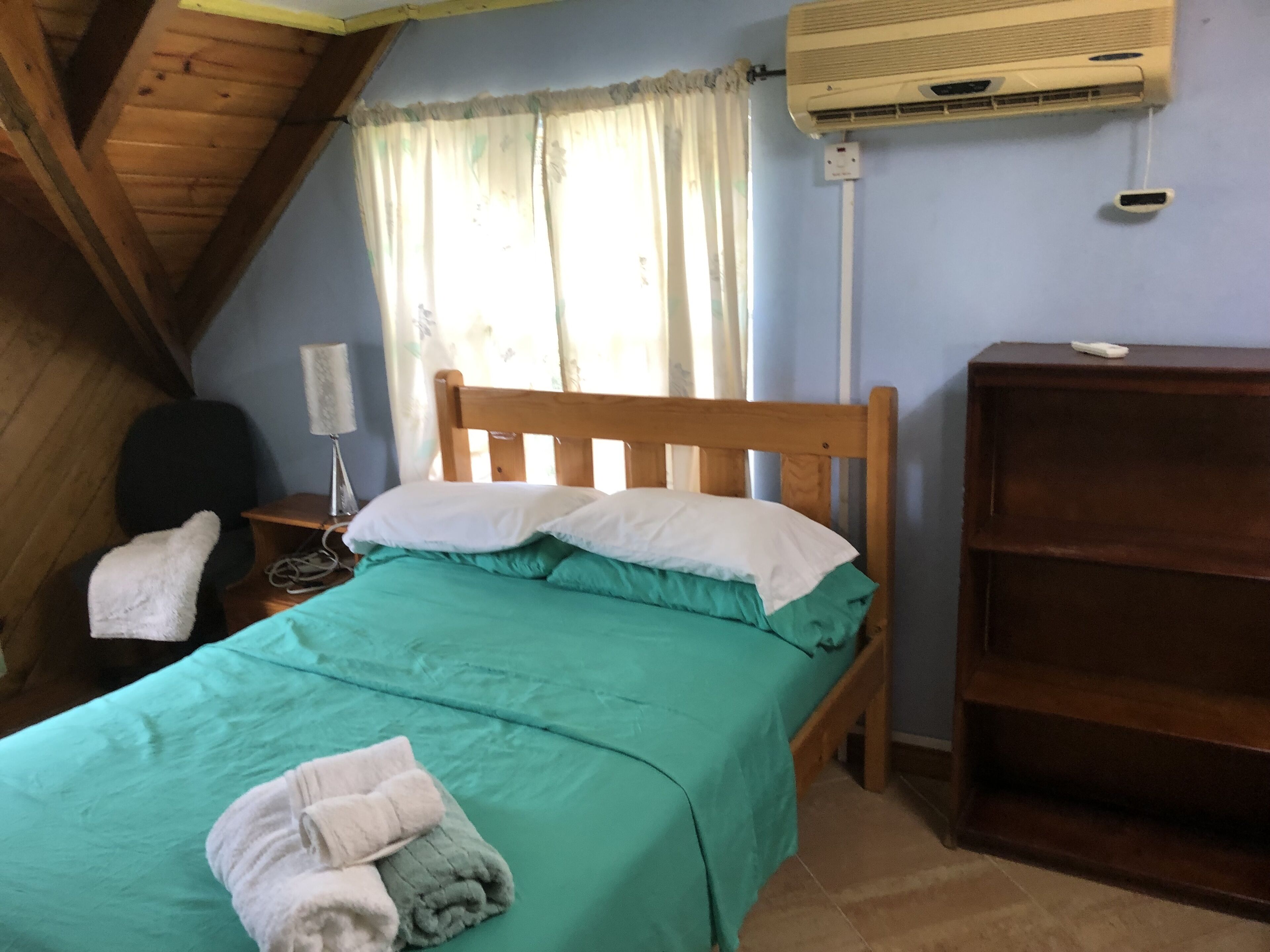 Un dormitorio con una cama de madera, un escritorio con lámpara, un armario y un equipo de aire acondicionado en la pared.